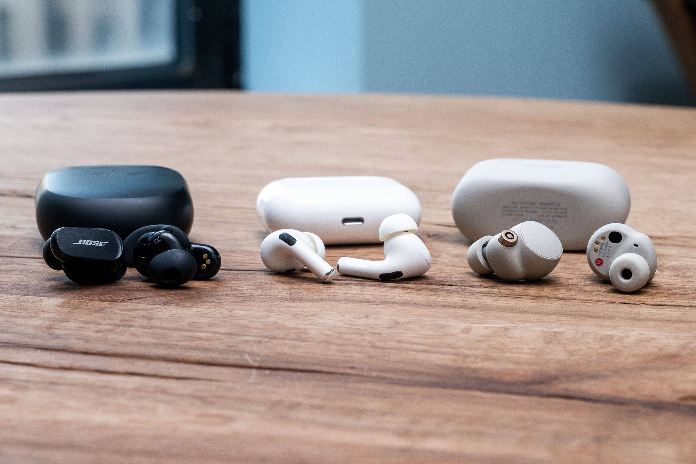 A side-by-side comparison photo of Bose's QuietComfort Earbuds II, Apple's AirPods Pro, and Sony's WF-1000XM4.