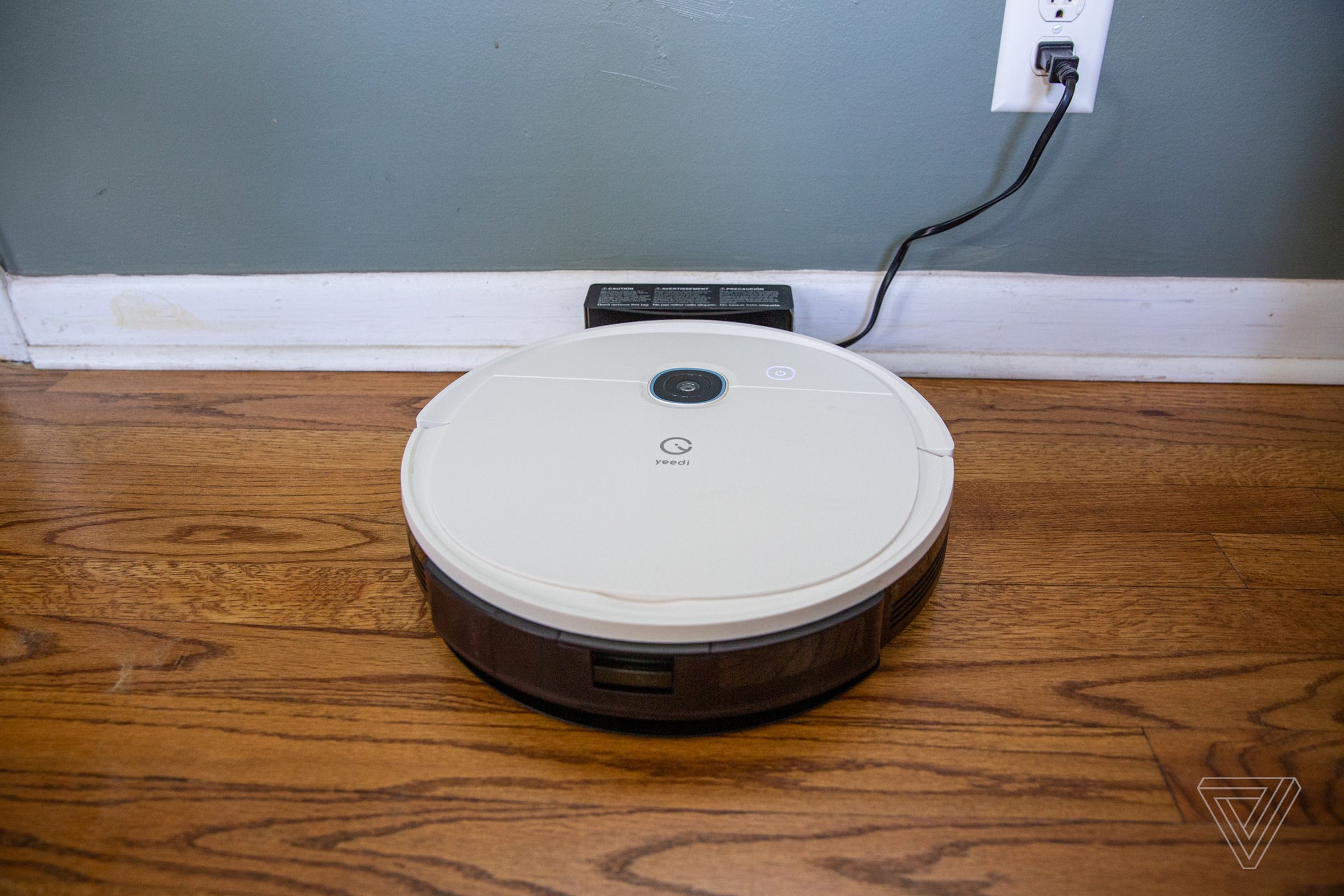 Yeedi's Vac 2 Pro robot vacuum cleaner sits on a hardwood floor and charges against a wall.