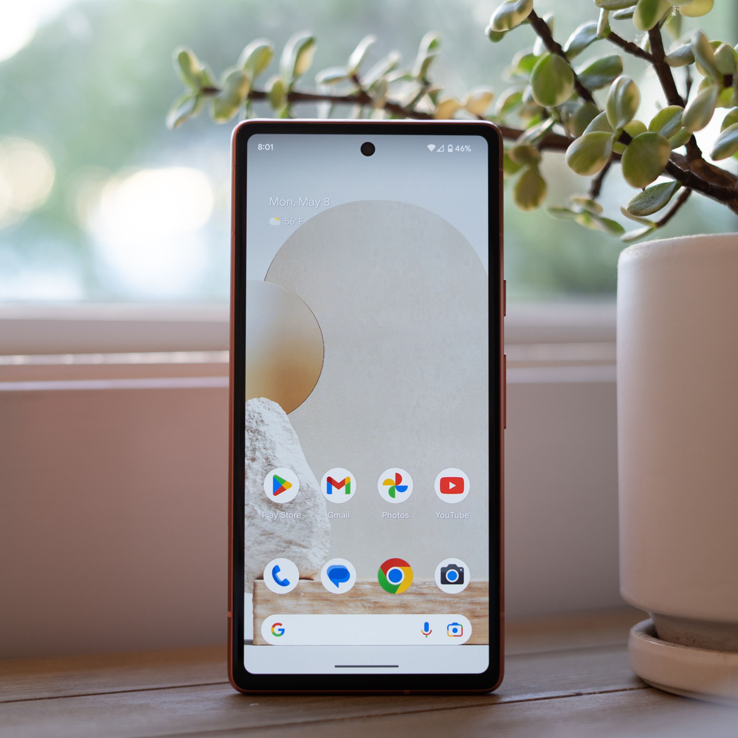 Google Pixel 7A standing upright on a table with home screen.